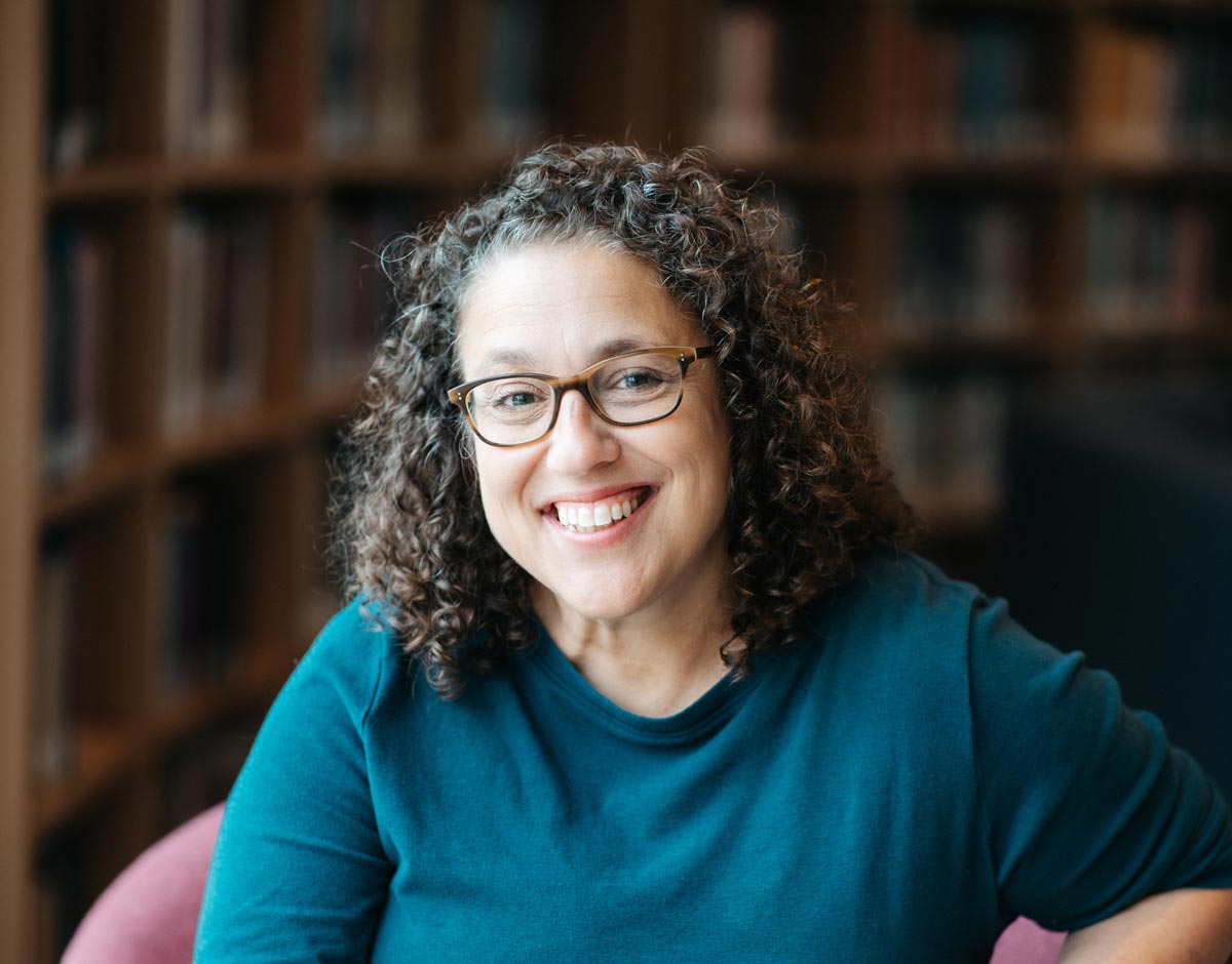 Professor Tropp smiles at the camera, in a turquoise shirt and glasses, in a library setting.